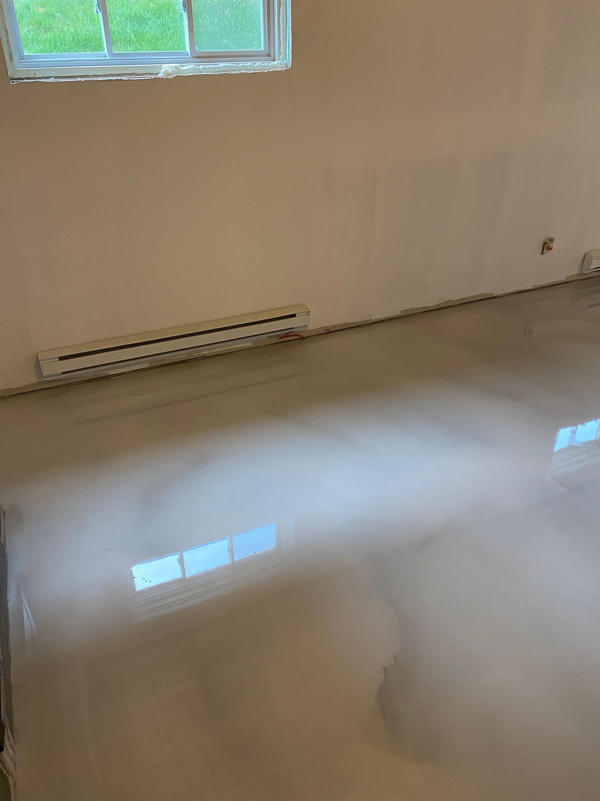 Une pièce avec un sol en béton brillant et une fenêtre.