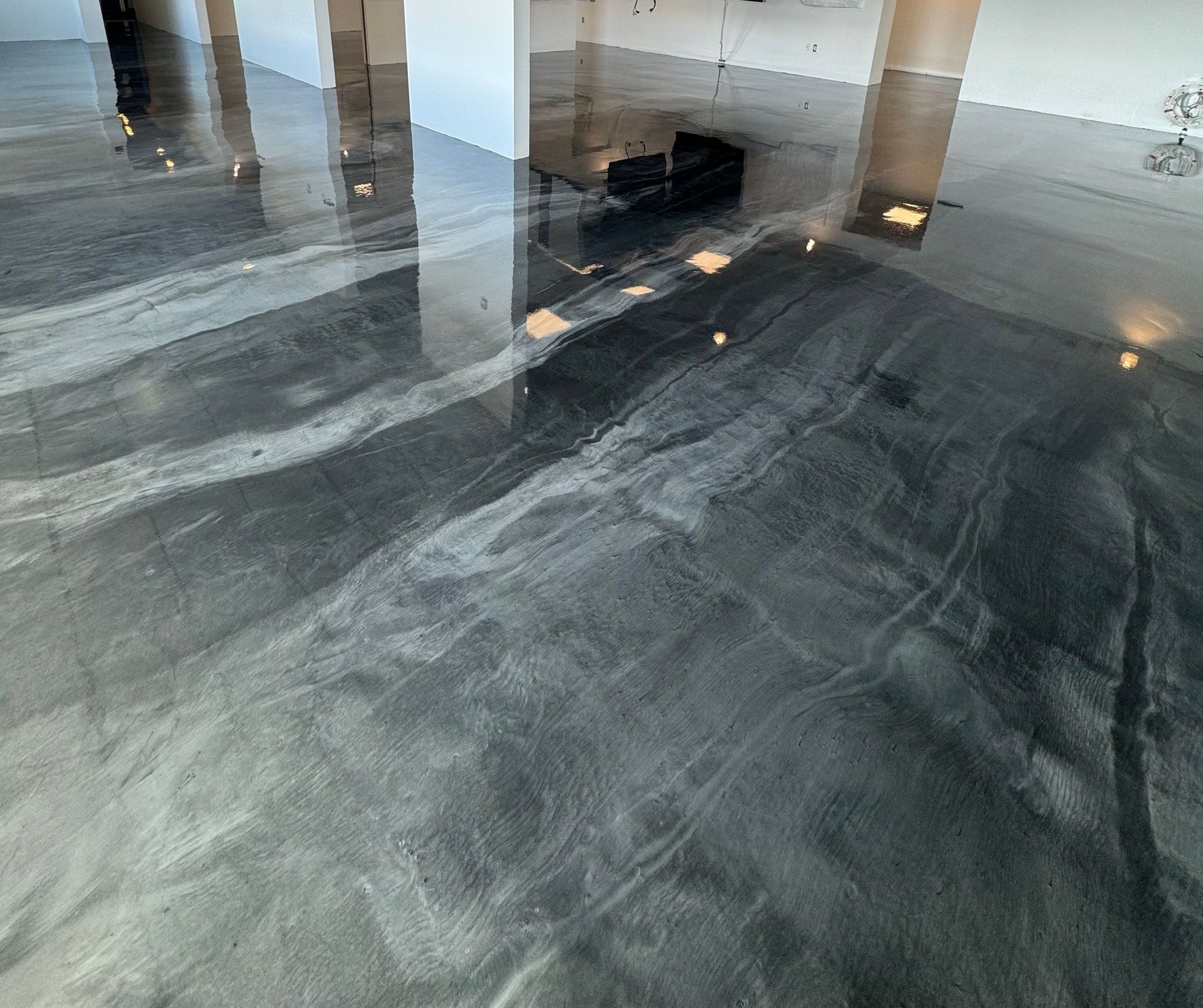 Sol en époxy gris métallisé brillant, orné de motifs tourbillonnants reflétant la lumière dans un espace moderne et ouvert.
