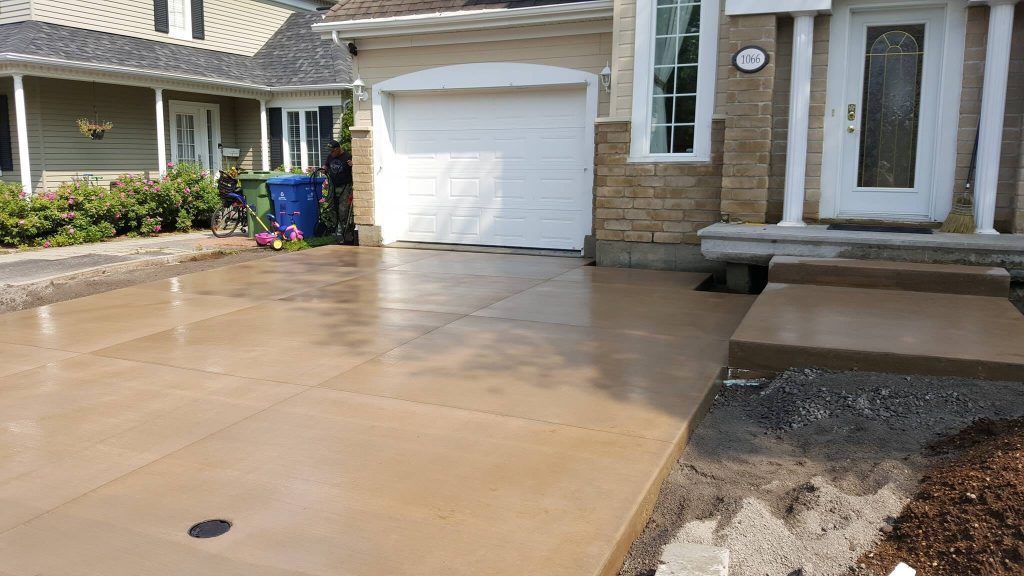 Une allée en béton devant une maison avec une porte de garage blanche.
