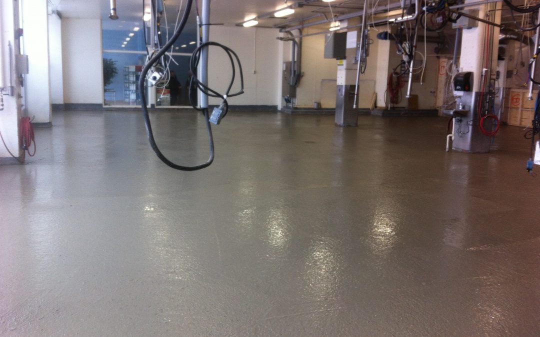 Une grande pièce avec un sol en béton et des tuyaux suspendus au plafond.