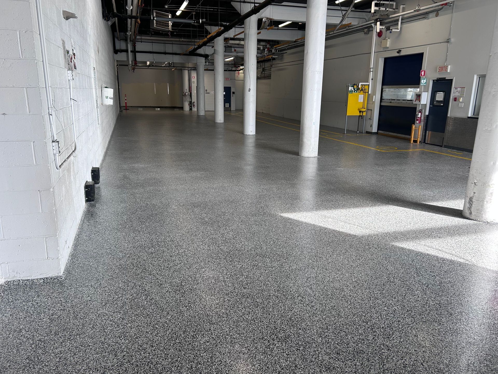 Une grande pièce vide avec un sol gris et des murs blancs.