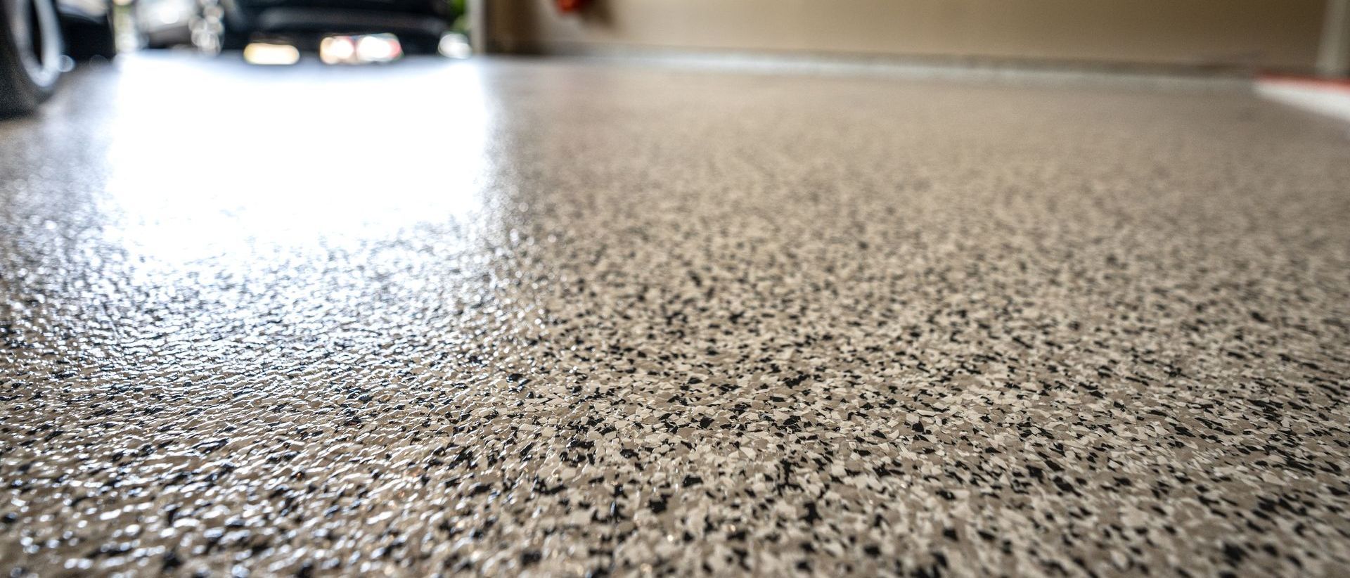 Un gros plan du sol d'un garage avec une voiture garée en arrière-plan.