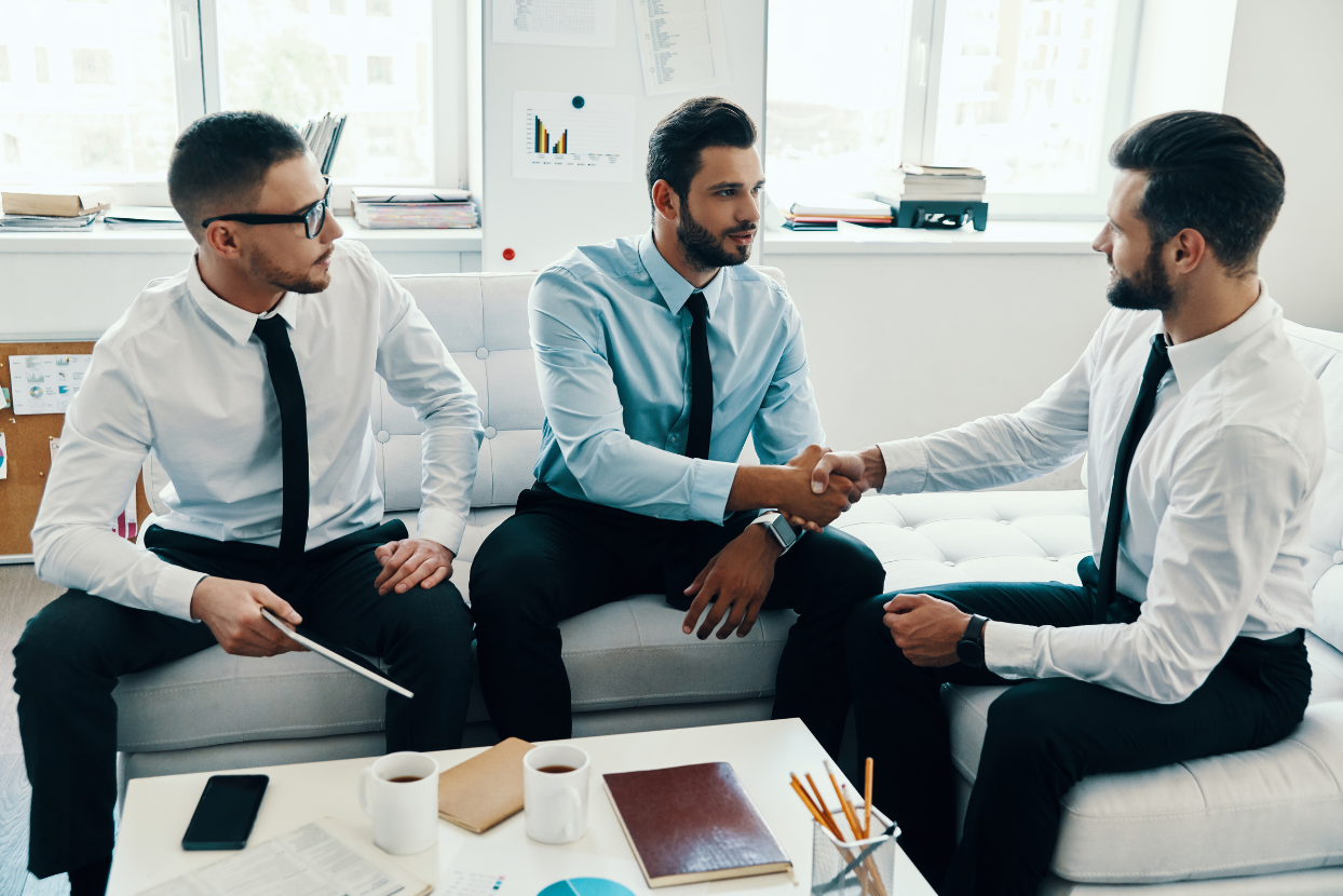 three businessmen are shaking hands while sitting on a couch .