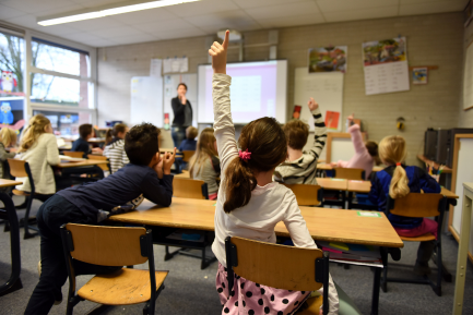 a girl is raising her hand in a classroom to answer a question .