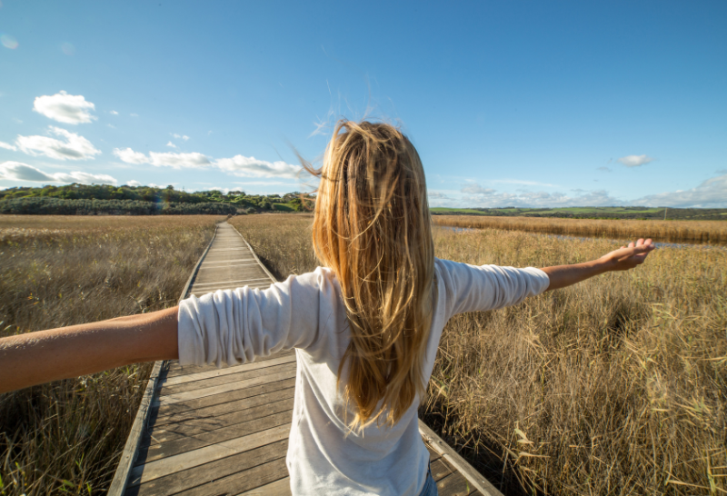 a woman is standing on a wooden walkway in a field with her arms outstretched .