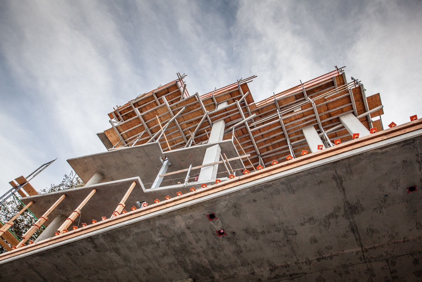 Construction site, low angle view of a building under construction, concrete and wood supports, cloudy sky.