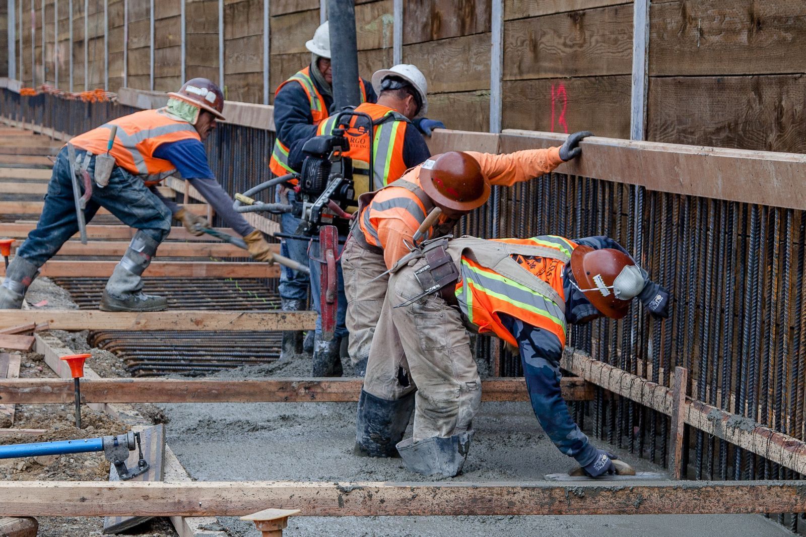 Construction workers pouring concrete, wearing hard hats and safety vests.