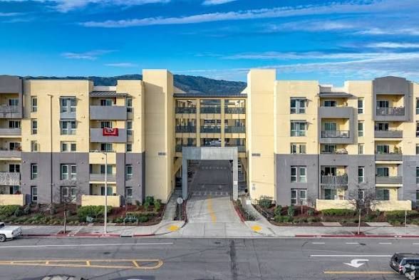 Apartment building with tan and gray exterior, entrance archway, and street in front.
