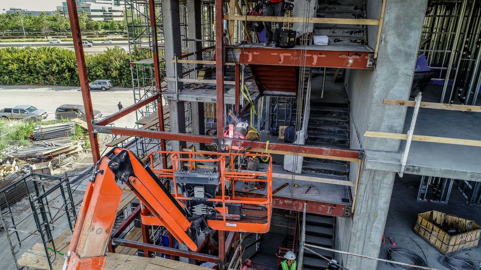 Construction site with orange lift, workers, and partially built concrete structure.