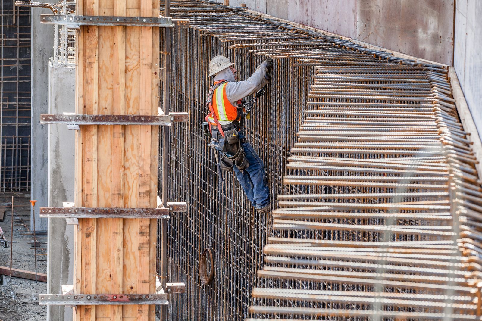 Construction worker in safety gear working on rebar framework near wooden formwork.