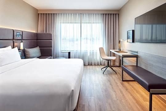 Hotel room with a bed, desk, and window with neutral colors.