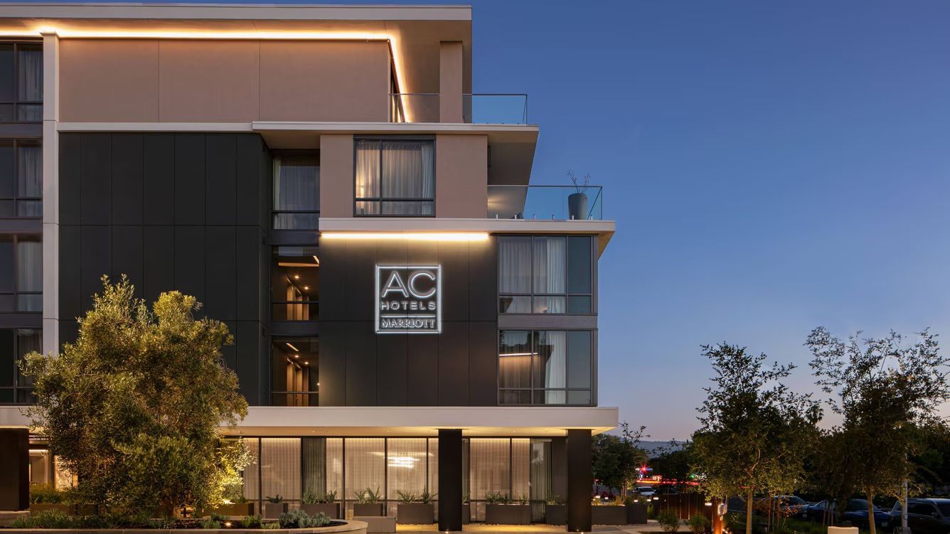 AC Hotel exterior at dusk, lit sign, dark facade, modern architecture.