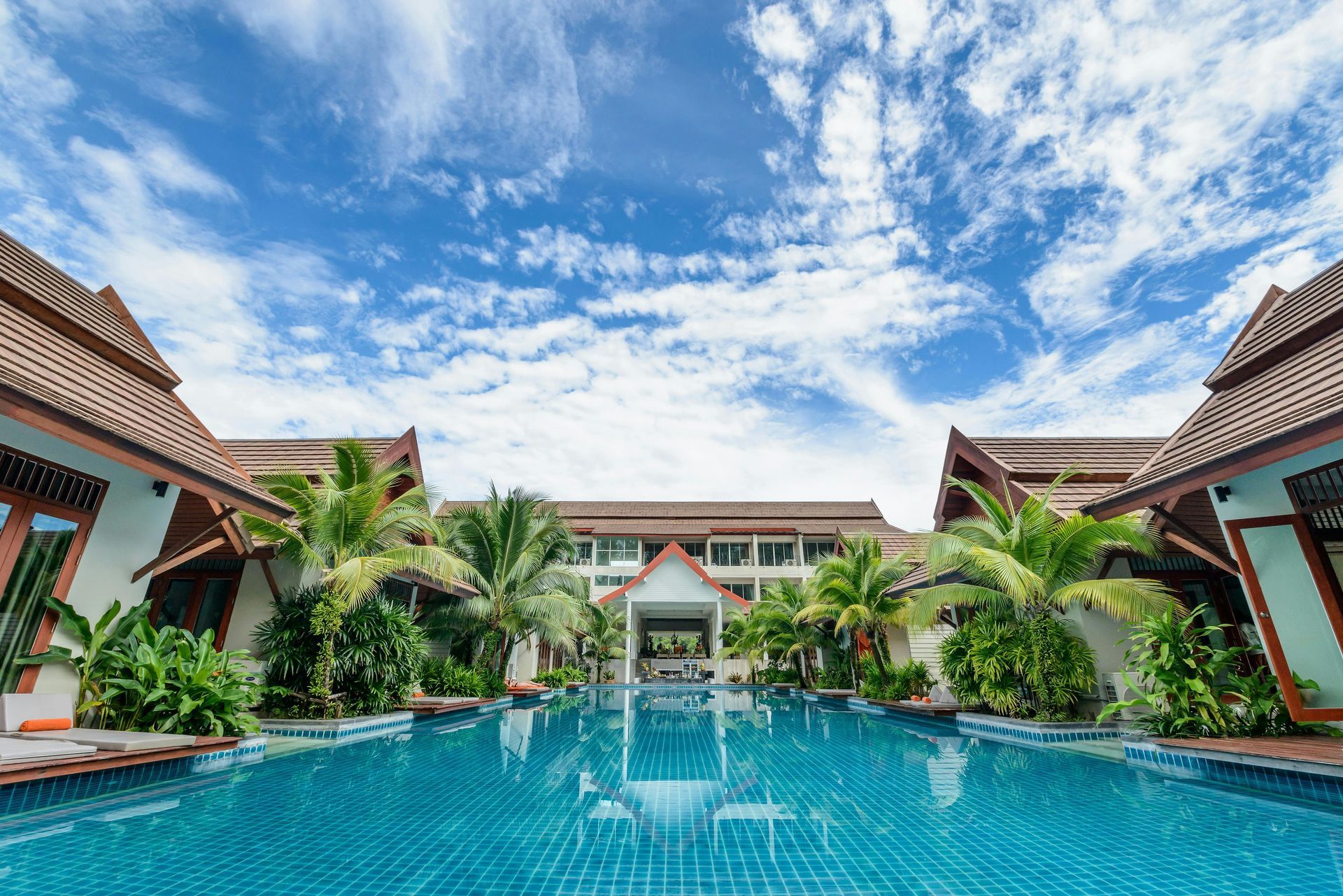 Swimming pool in front of a resort with blue sky and white clouds.
