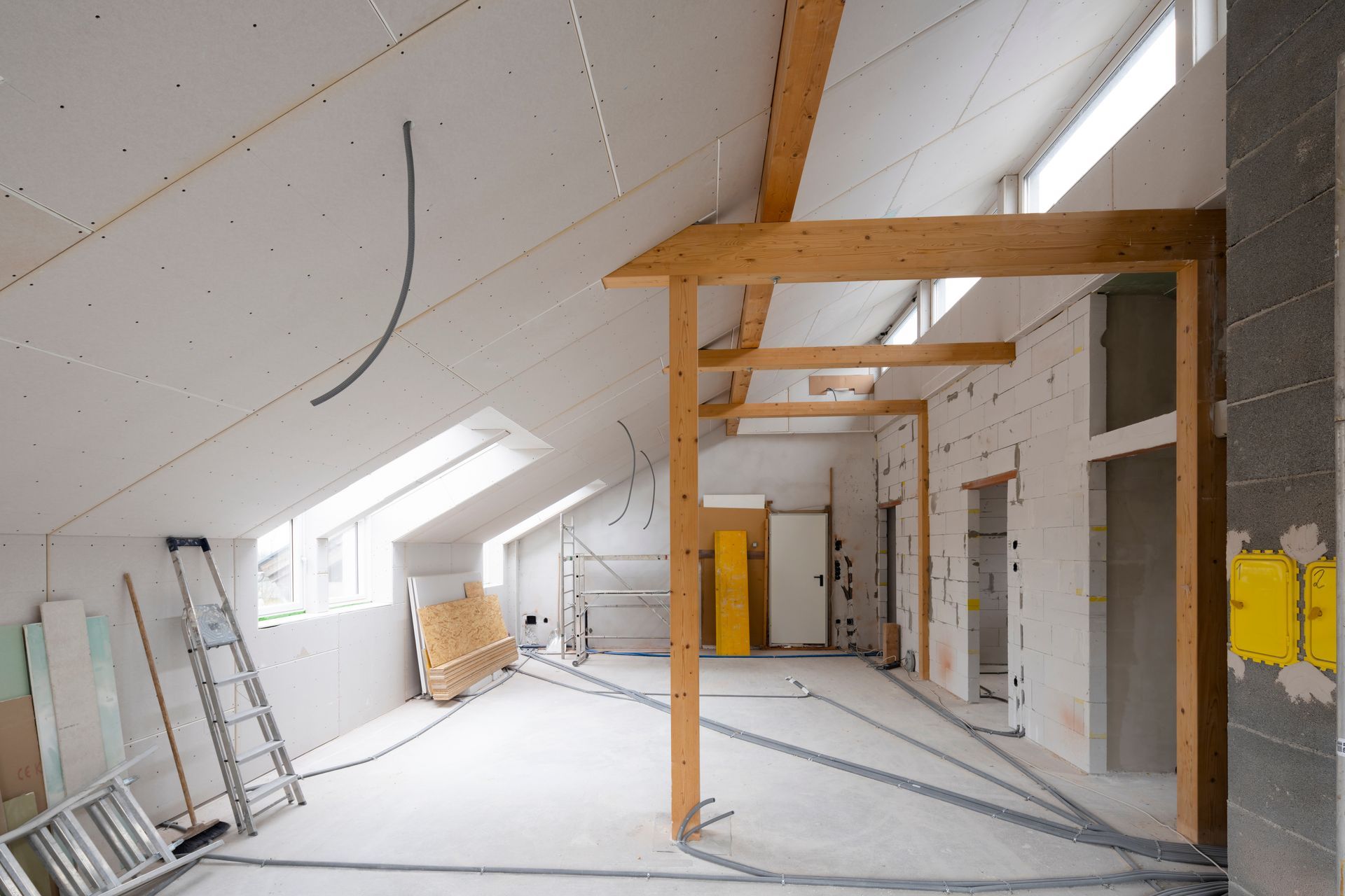A person using a long metal tool to smooth wall plaster against a ceiling. They are standing in a room.