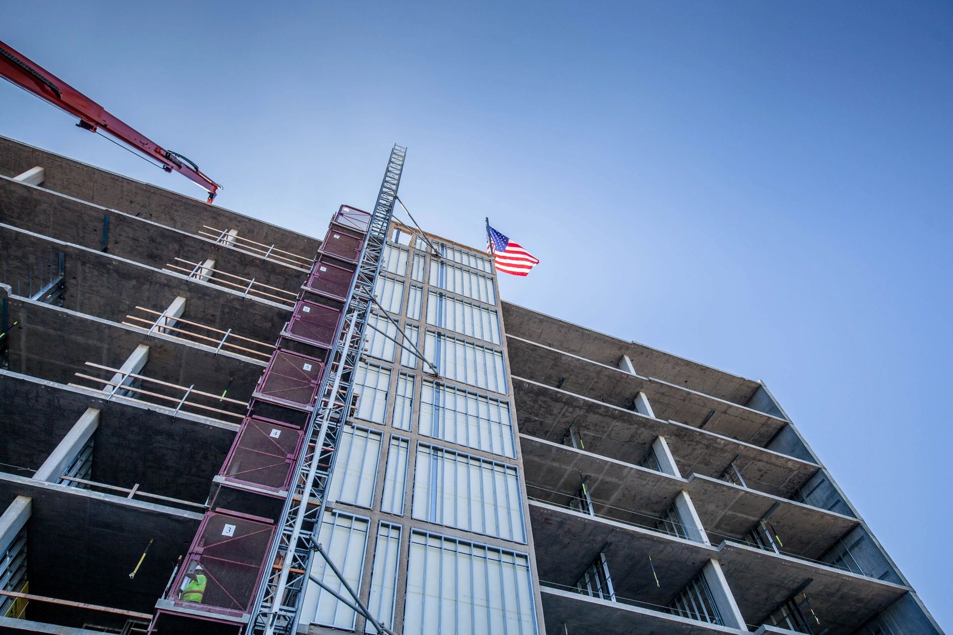Construction of a high-rise building with an American flag waving in the sun.