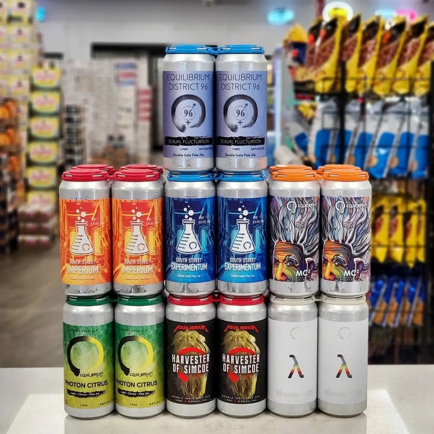 A stack of colorful beverage cans displayed on a store counter; various designs and colors.