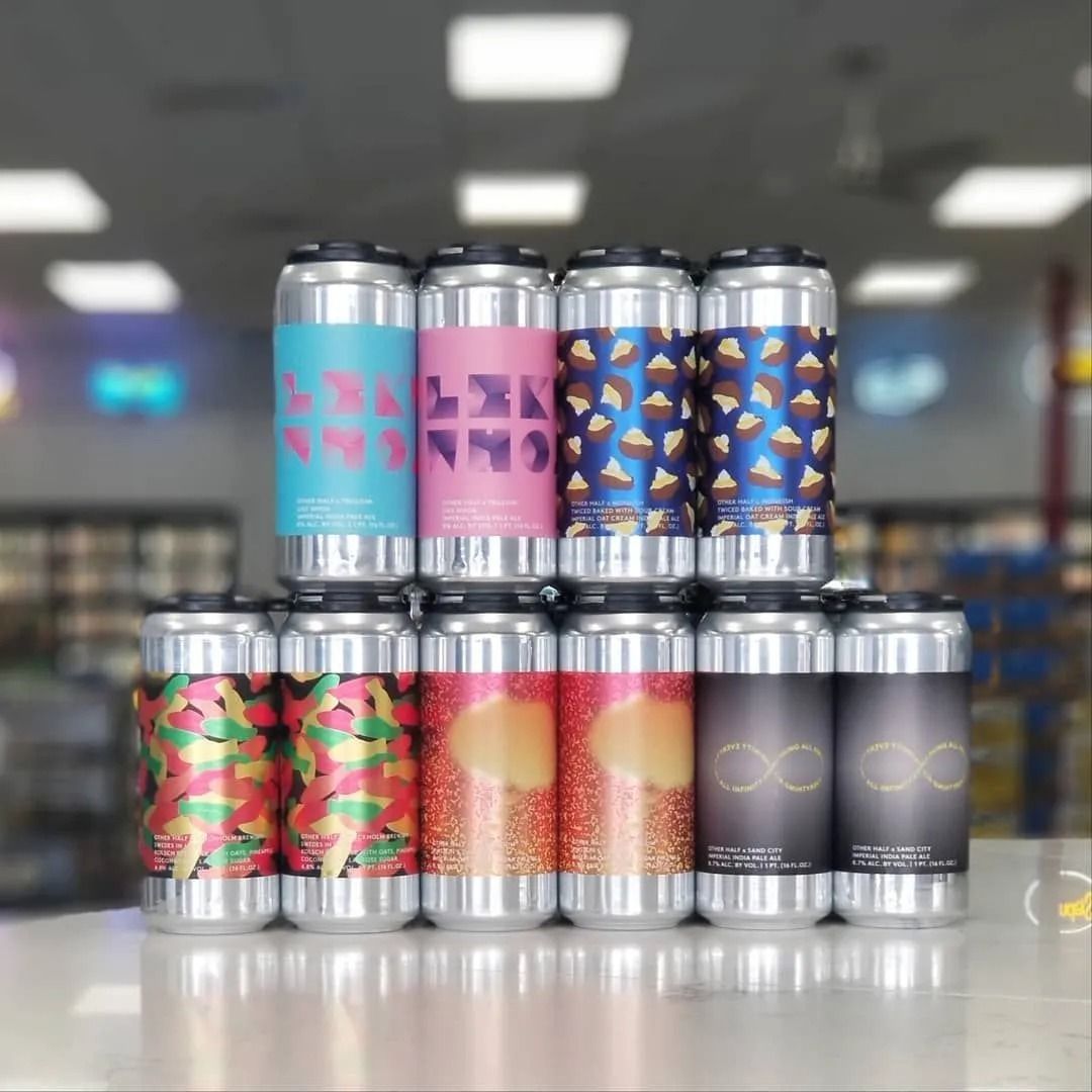 A stack of colorful beer cans on a counter. Different patterns and colors on the labels, inside a store.