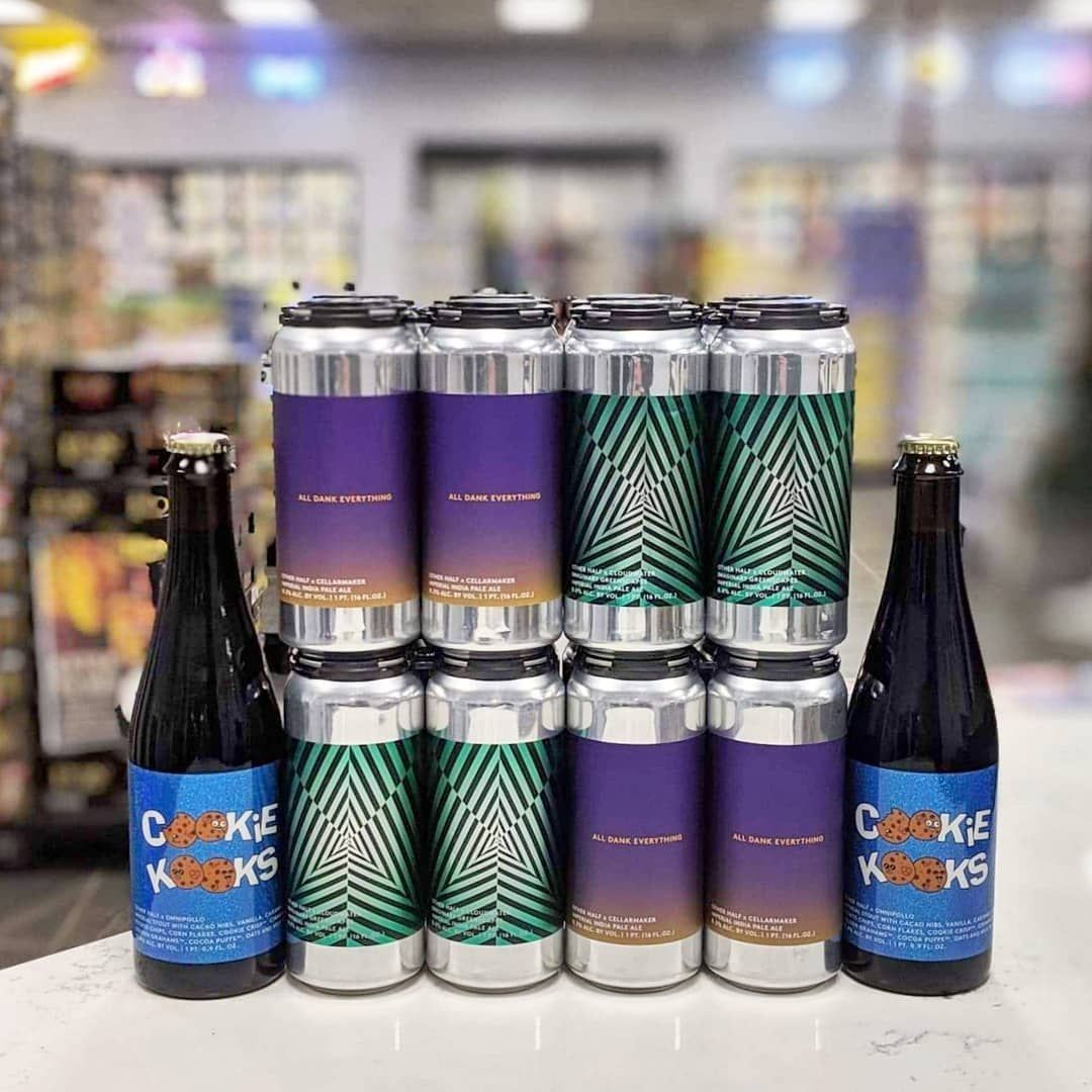 Two dark glass bottles and a stack of colorful beer cans on a counter in a store.