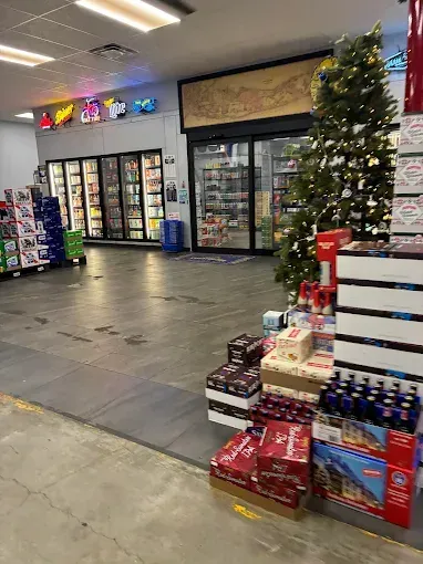 Interior of a store, several refrigerated doors, Christmas tree, and displays of beverages and gifts.