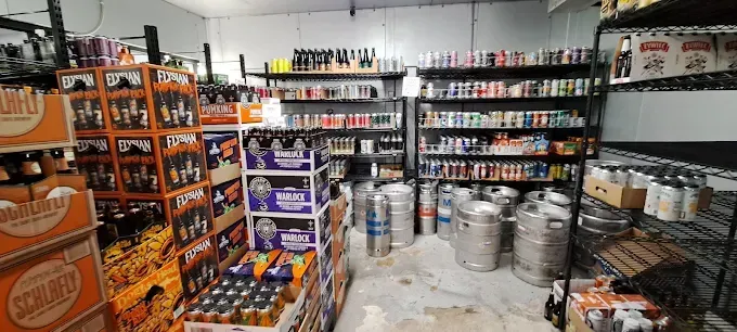 A beer store interior with multiple shelves of canned and bottled beverages, and several kegs on the floor.