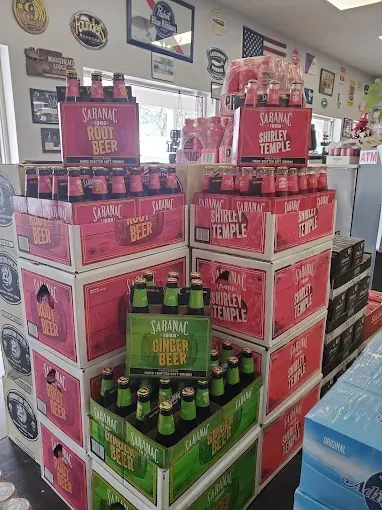 Stacked boxes of Saranz root beer, Shirley Temple, and ginger beer in a store display.