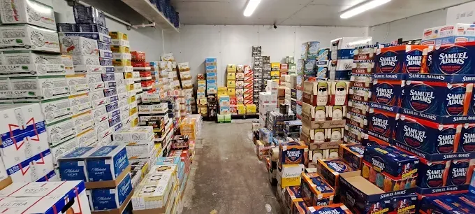 Aisle in a beverage warehouse lined with stacked boxes of beer, a colorful display in the middle.