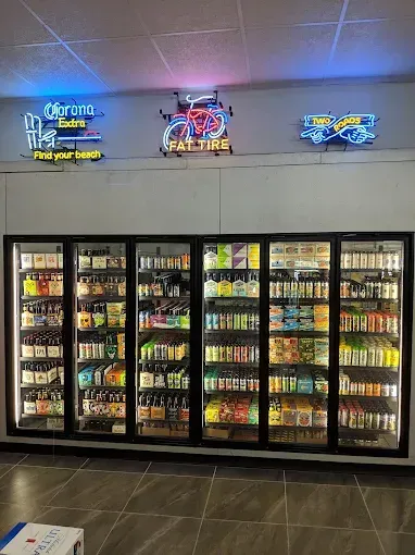 Beer coolers with neon signs above. Blue and red neon signs hang above a row of glass-fronted refrigerators.