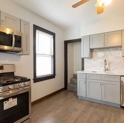 Modern kitchen with gray cabinets, stainless steel appliances, white tile backsplash, and a window