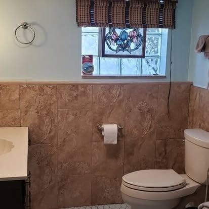 Small bathroom with toilet, window, and brown tiled walls.