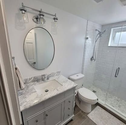 Bright modern bathroom with marble vanity, round mirror, glass shower, and window.