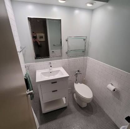 Small modern bathroom with white sink, toilet, mirror, and gray tile walls and floor.