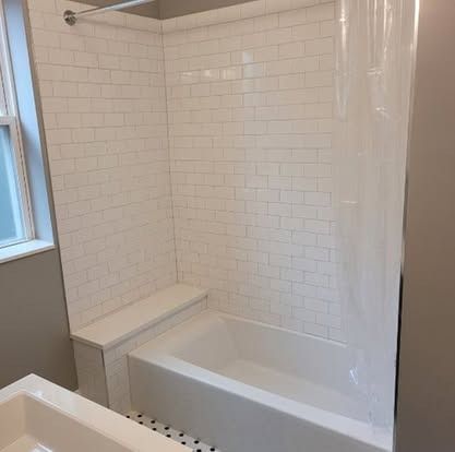 Small bathroom with a white subway-tile tub surround, built-in ledge, and window.
