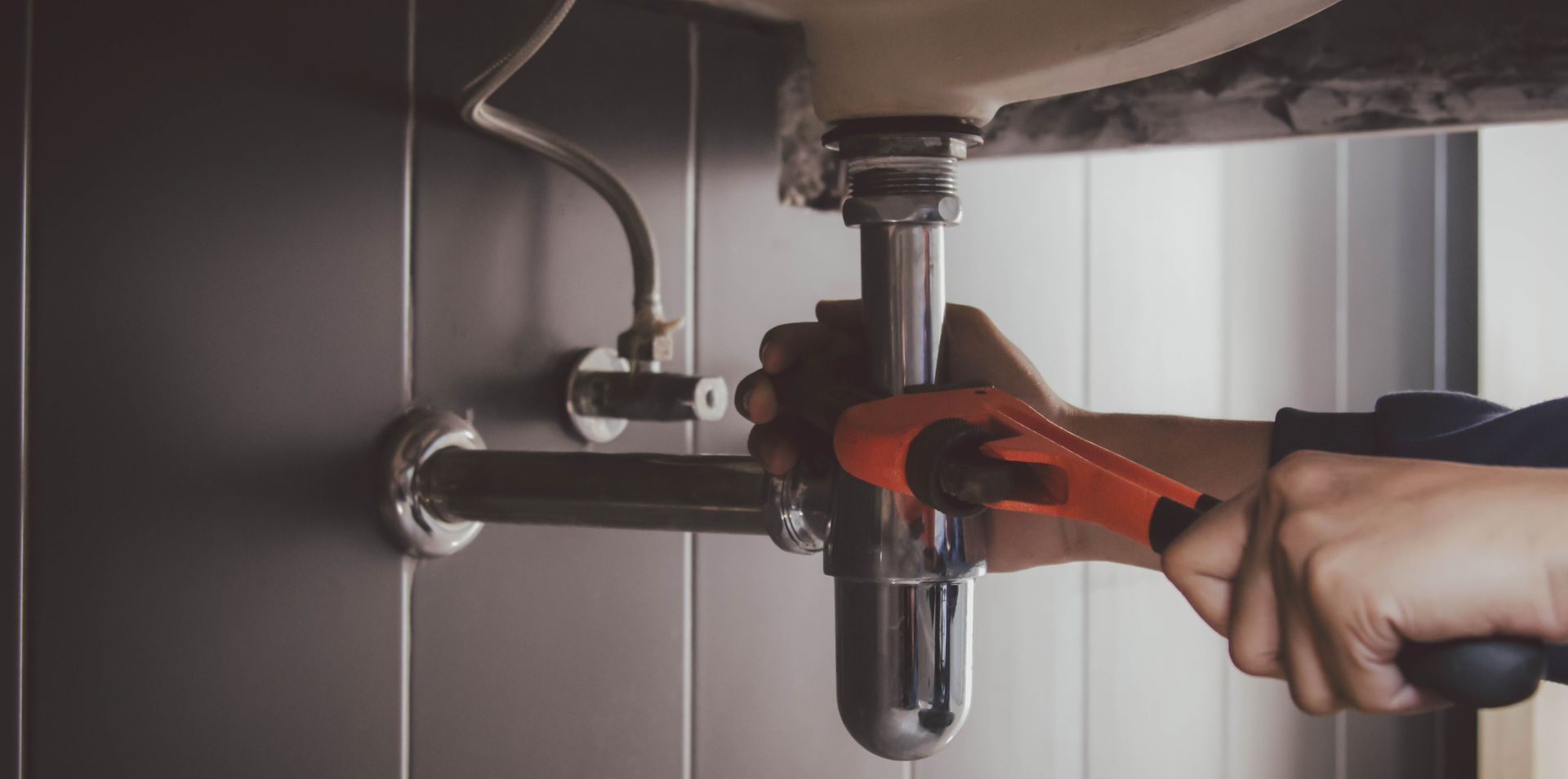 Person using a red pipe wrench to tighten plumbing under a sink