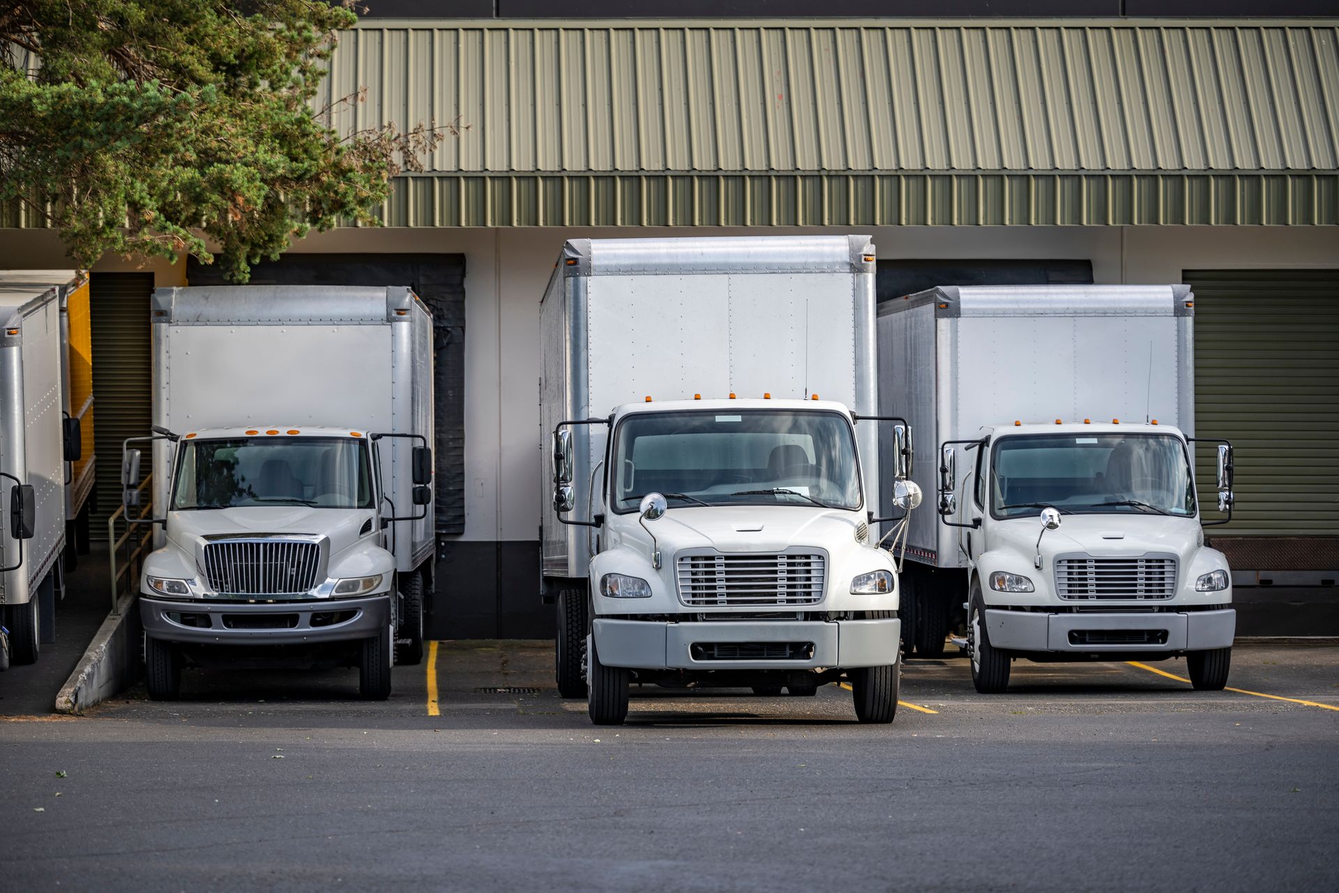 Three white trucks are parked in front of a warehouse.