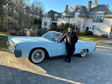 A man is standing next to a white car in front of a house.