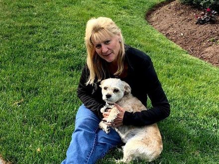 A woman is sitting on the grass holding a small dog.