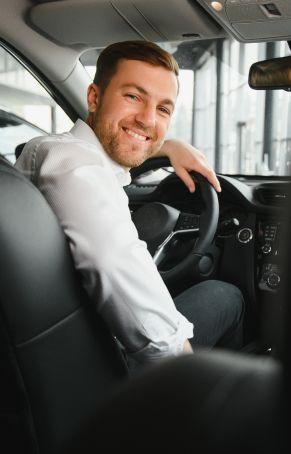 A man is sitting in the driver 's seat of a car and smiling.