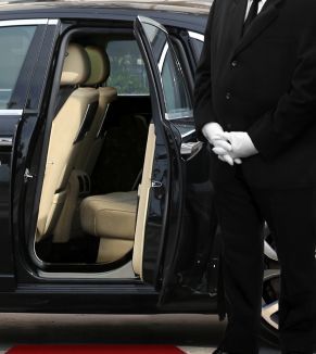 A man in a suit is standing next to a car with the door open