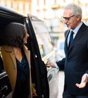 A man in a suit and tie is helping a woman out of a car.