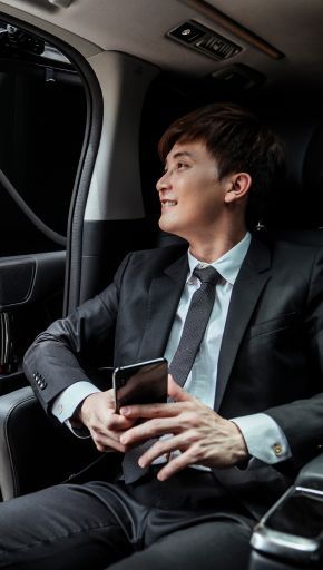 A man in a suit and tie is sitting in the back seat of a car holding a cell phone.