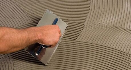 A Person is Applying Adhesive to a Tile Floor With a Trowel — Northern Tile Gallery in Winnellie, NT