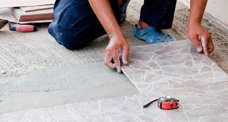 A Man is Kneeling Down to Install a Tile Floor — Northern Tile Gallery in Winnellie, NT