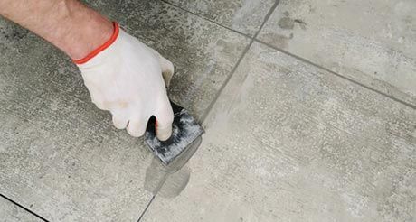A Person is Using a Spatula to Spread Concrete on a Tiled Floor — Northern Tile Gallery in Winnellie, NT