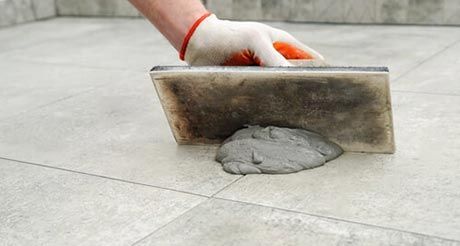 A Person is Spreading Cement on a Tile Floor With a Trowel — Northern Tile Gallery in Winnellie, NT