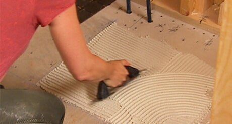 A Person is Laying Tile on the Floor With a Trowel — Northern Tile Gallery in Winnellie, NT