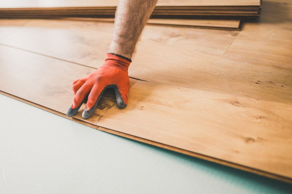 A Man Wearing Orange Gloves is Installing a Wooden Floor — Northern Tile Gallery in Winnellie, NT