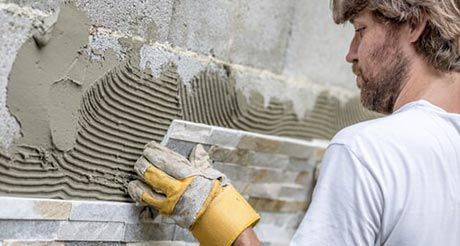 A Man is Laying Tiles on a Wall With a Trowel — Northern Tile Gallery in Winnellie, NT