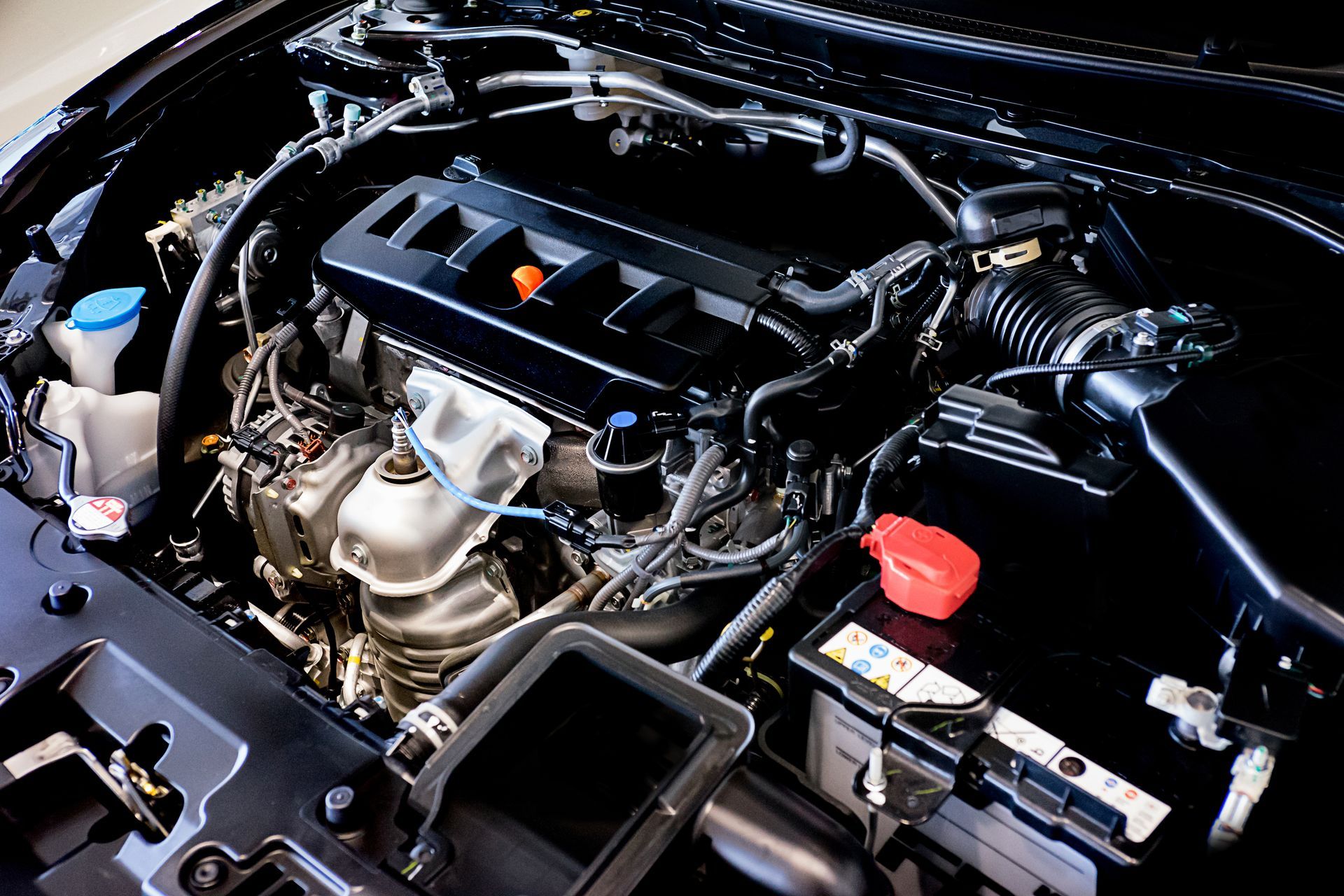 Car engine bay with black engine cover and visible battery, hoses, and components Car engine bay with black engine cover and visible battery, hoses, and components
