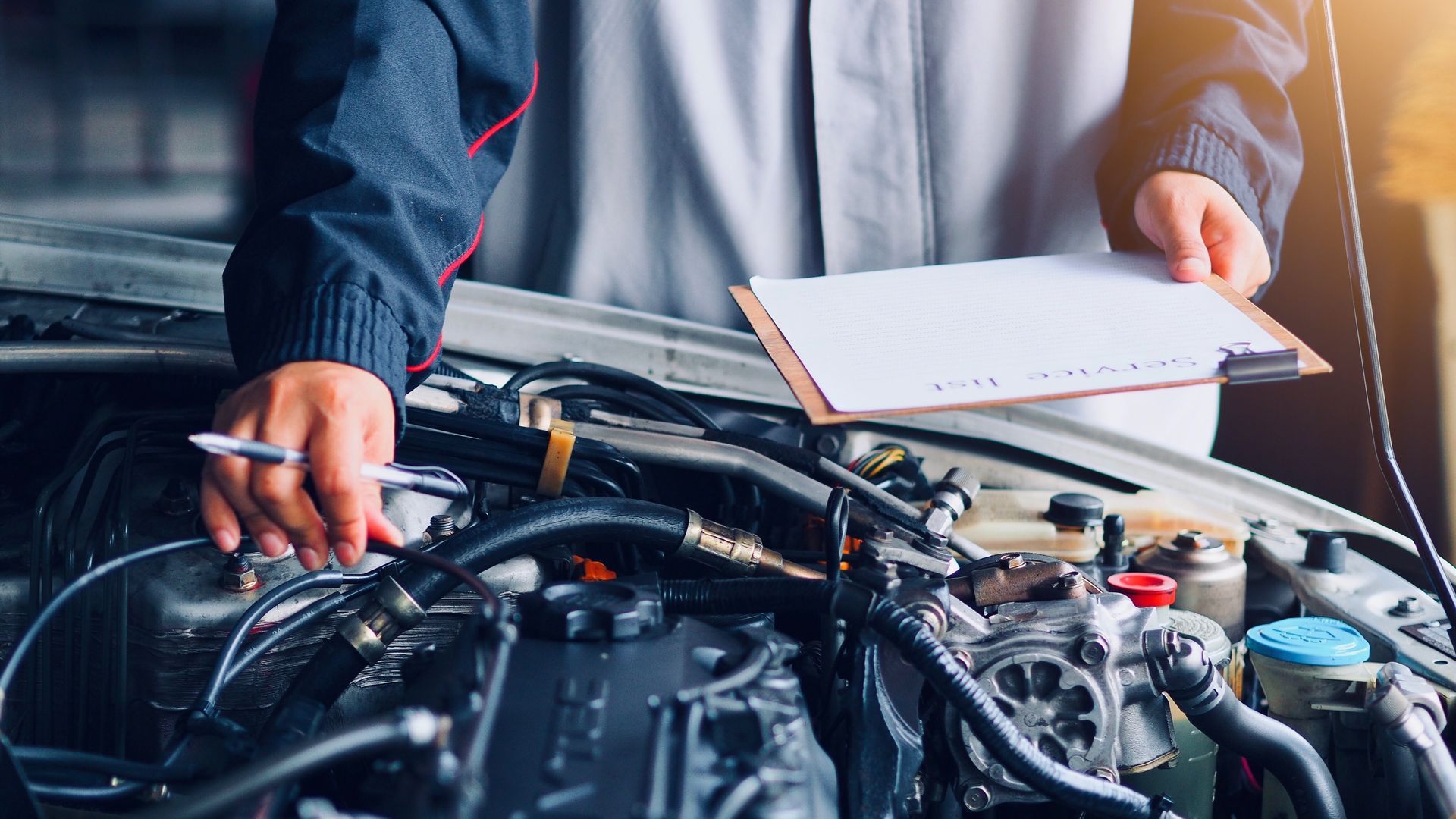 Mechanic inspecting an open car engine with a clipboard in a repair shop Mechanic inspecting an open car engine with a clipboard in a repair shop