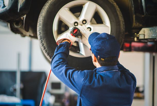 Mechanic using a wrench on a raised car wheel in an auto shop Mechanic using a wrench on a raised car wheel in an auto shop